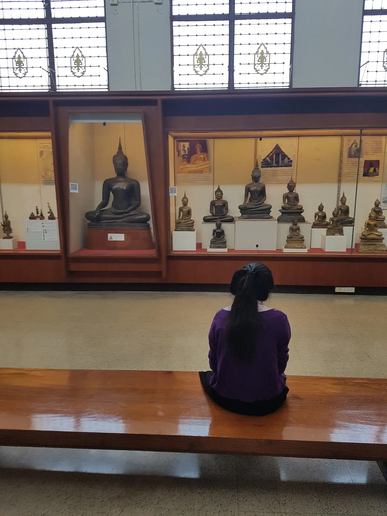 ผู้เข้าชมดูพระพุทธรูปในตู้กระจกที่อาคาร 1 พิพิธภัณฑสถานแห่งชาติเจ้าสามพระยา ภาพถ่ายปี 2560 จาก Wikimedia Commons (Iudexvivorum, CC0)