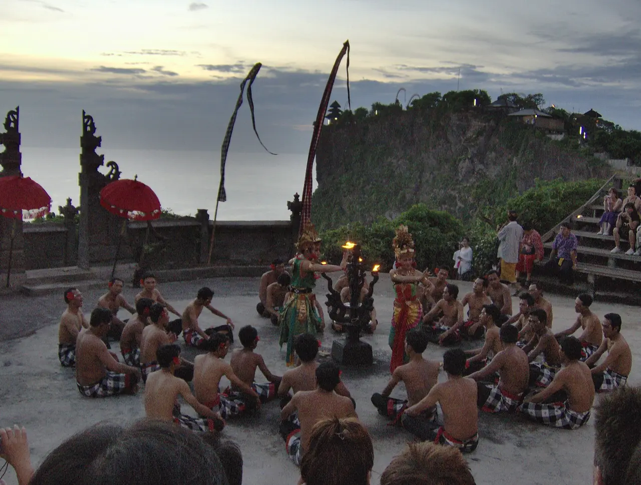 ลานแสดงเคจักที่วัดอูลูวาตู มีประตูหินสูงอยู่ด้านหลังและผู้ชมนั่งล้อมวง (ภาพช่วงเริ่มการแสดง)