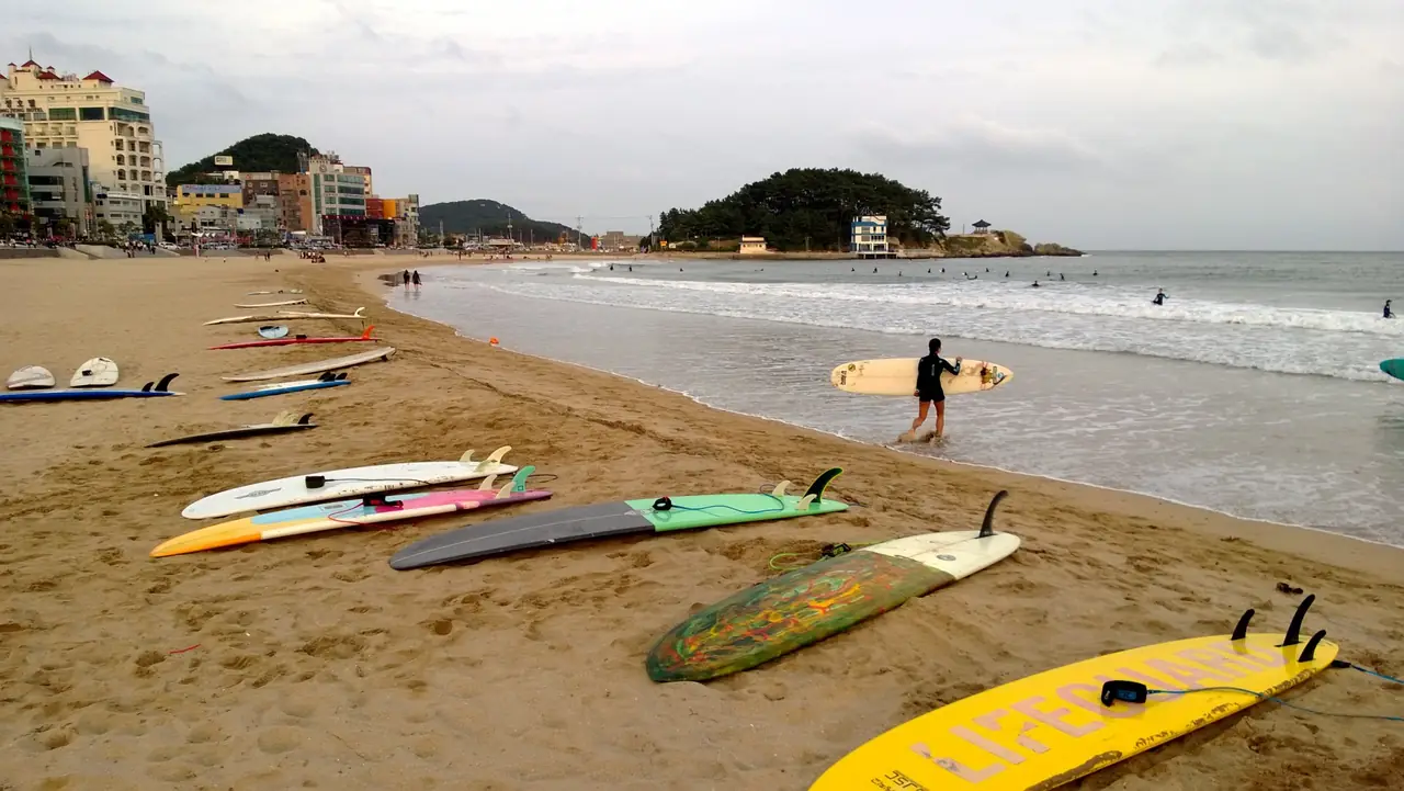 หาดซงจองตอนเย็น มีกระดานโต้คลื่นวางบนทราย ปลายทางหนึ่งของรถไฟชายหาด