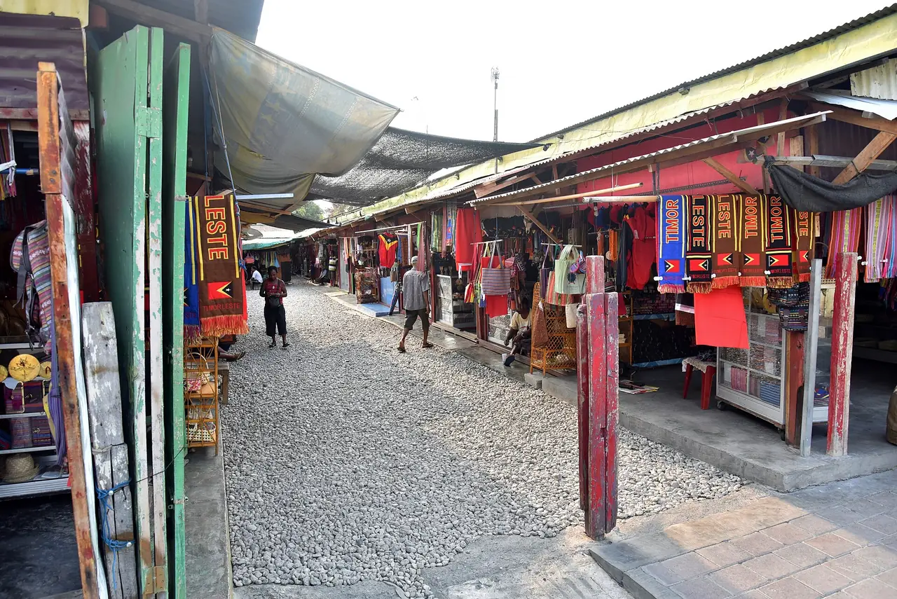 ทางเดินระหว่างแผงขายผ้าทอในตลาดทาอิสของดิลี ภาพจาก Wikimedia Commons ผู้ถ่าย Bahnfrend สัญญา CC BY-SA 4.0 ถ่ายปี 2018 ตามชื่อไฟล์
