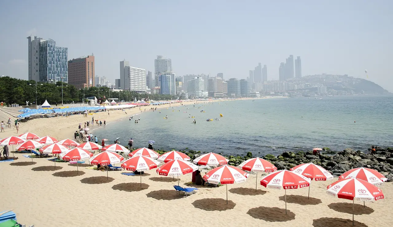 หาดแฮอุนแด มีร่มสีแดงขาวบนทรายและตึกสูงของย่านแฮอุนแดอยู่ไกลออกไป