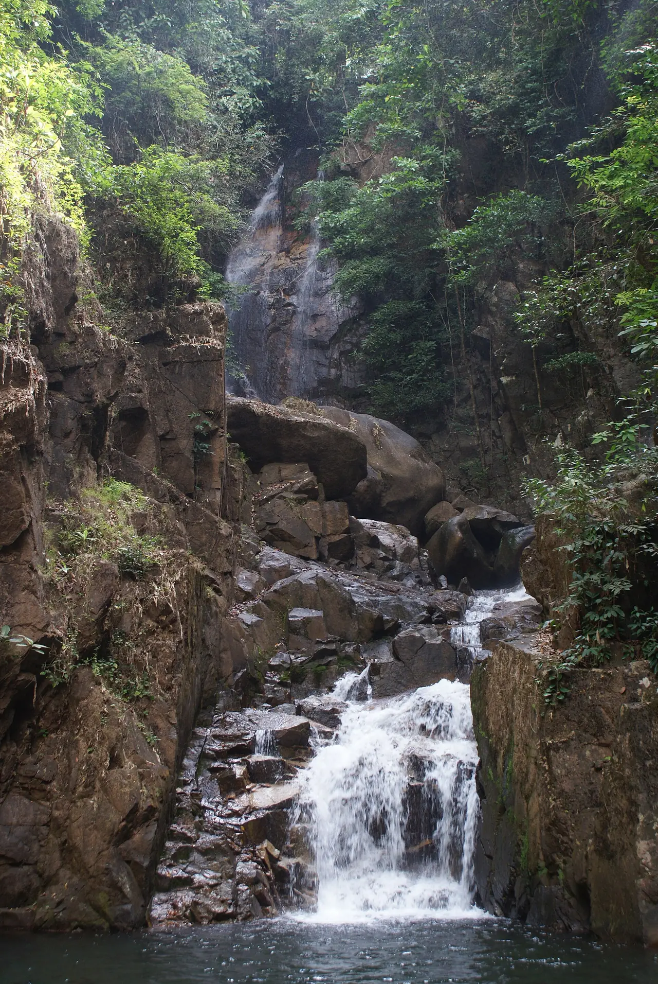 A waterfall dropping over dark rock into a pool at Namtok Phliu National Park