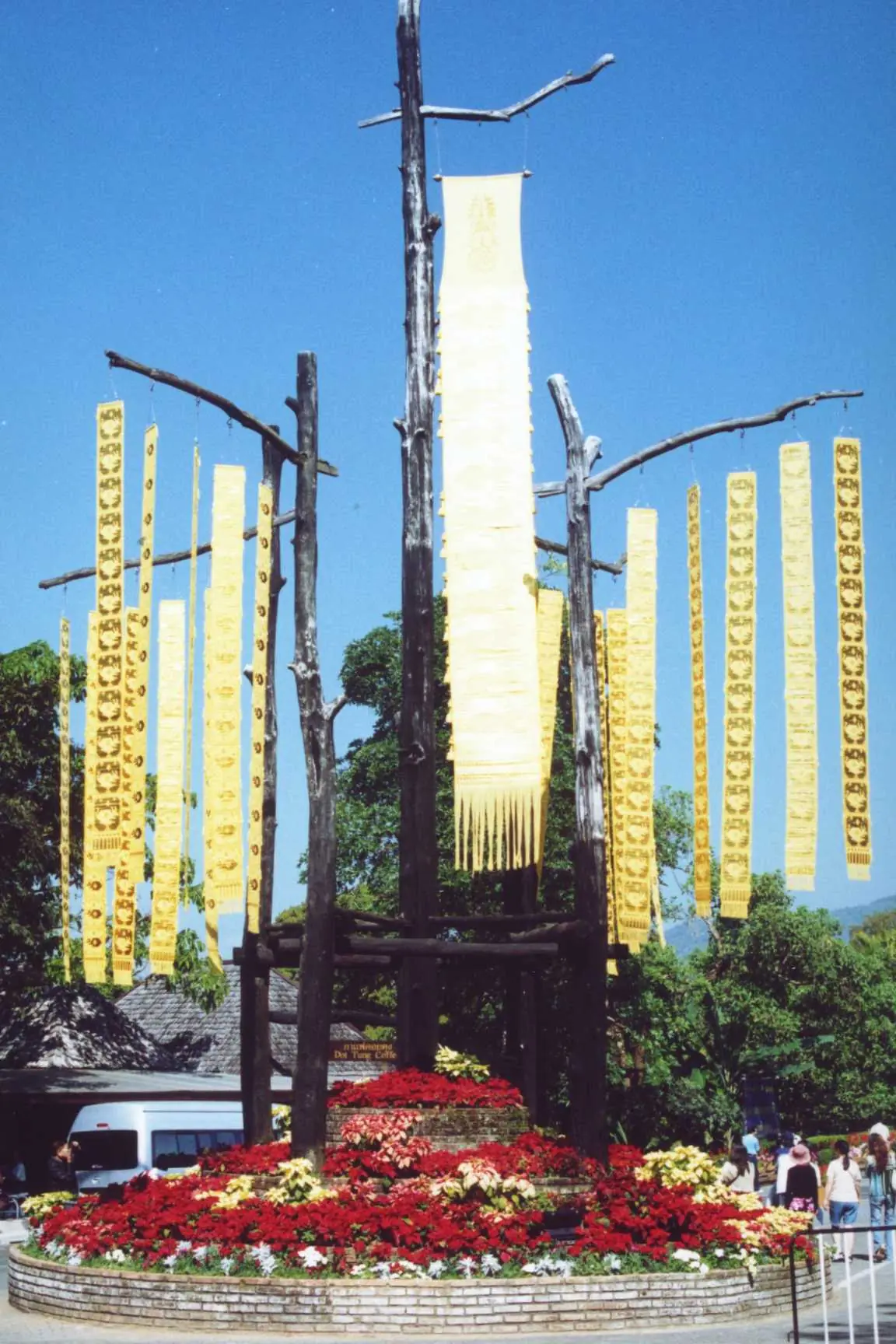 ตุงล้านนาสีทองและแปลงดอกไม้แดงบริเวณพระตำหนักดอยตุง ภาพถ่ายจาก Wikimedia Commons (Ahoerstemeier) ไม่ระบุปีที่ถ่าย