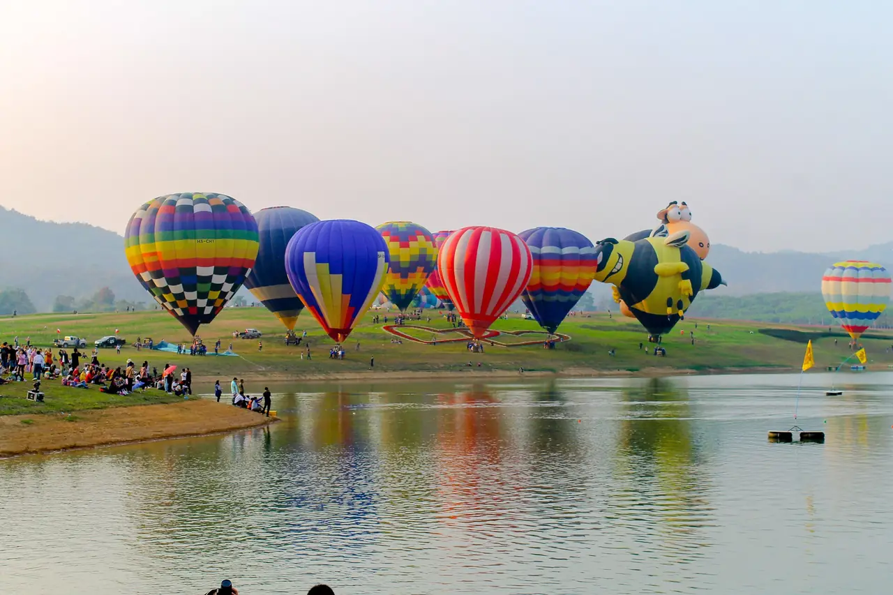 บอลลูนหลายลูกลอยเหนือสนามหญ้าและทะเลสาบในงาน Singha Park International Balloon Fiesta ภาพถ่ายจาก Wikimedia Commons (Natthaphong Kaewruecha)