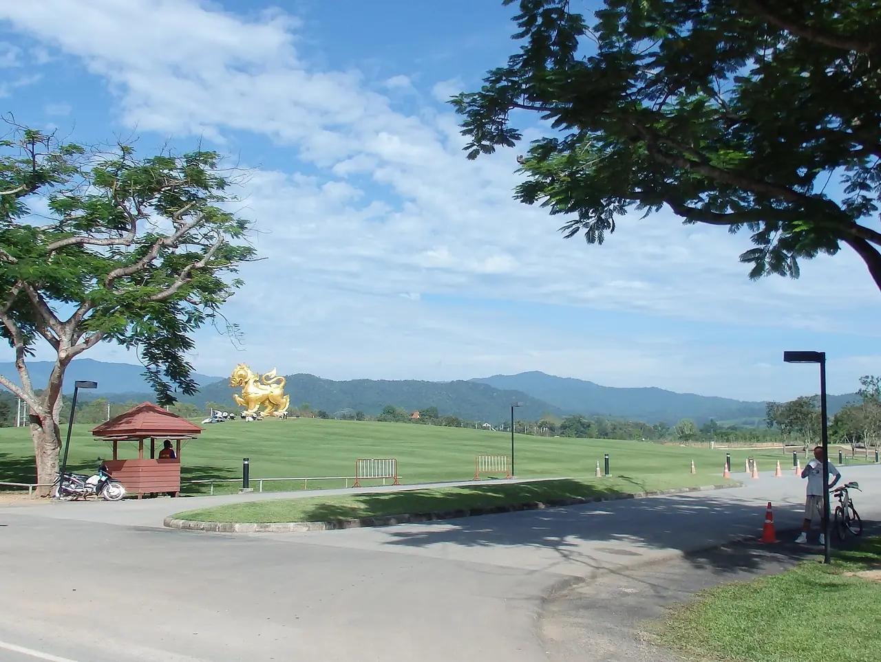 ทุ่งหญ้าและรูปปั้นสิงห์สีทองในย่านตำบลแม่กรณ์ ภาพถ่ายจาก Wikimedia Commons (mohigan จากชุดภาพ panoramio) คำอธิบายภาพไม่ระบุว่าเป็นสิงห์ปาร์ค ภาพประกอบ