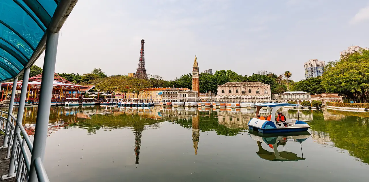 ทะเลสาบในสวน Window of the World มีเรือถีบ และมีเจดีย์หอไอเฟลกับหอระฆังแบบเวนิสจำลองอยู่เบื้องหลัง ภาพจาก Wikimedia Commons ผู้ถ่าย Dinkun Chen สัญญา CC BY-SA 4.0 ภาพมุมกว้างหลายช่องแสง