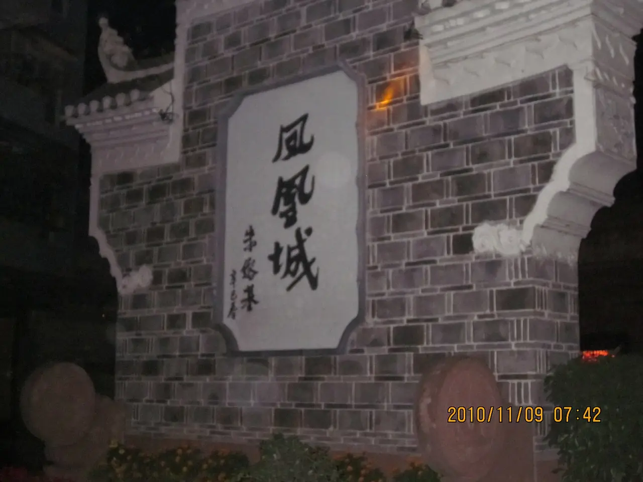 ป้ายอักษร "เมืองเฟิ่งหวง" บนกำแพงอิฐ ถ่ายตอนกลางคืนวันที่ 9 พ.ย. 2553 ตามเวลาในภาพ ภาพจาก Wikimedia Commons ผู้ถ่าย Huangdan2060 สัญญา CC0 เป็นภาพเก่าและค่อนข้างมืด