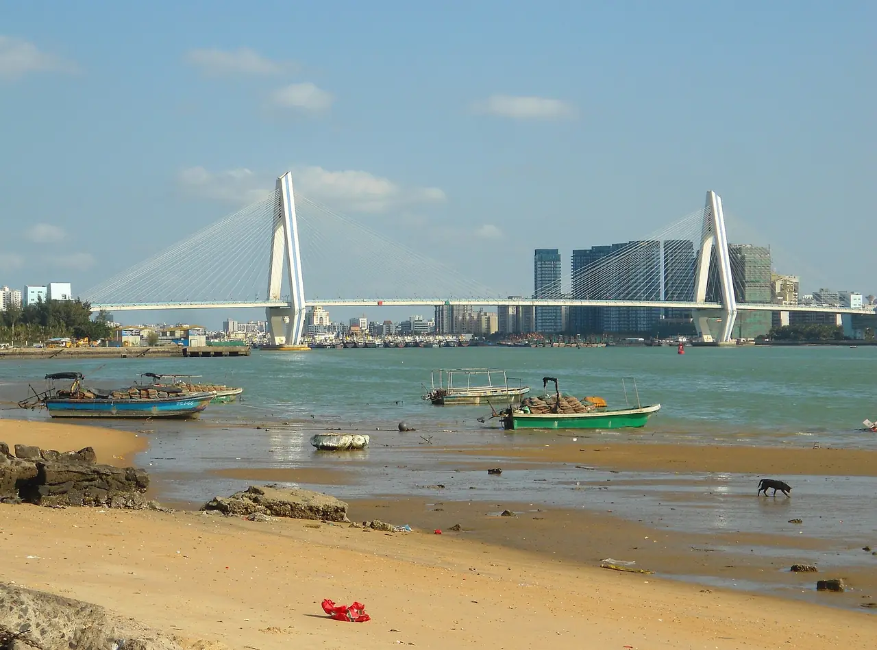 สะพานแม่น้ำไห่เตี้ยนมองจากชายหาดเกาะไห่เตี้ยน ฝั่งตรงข้ามเห็นตัวเมืองไหโข่ว ภาพจาก Wikimedia Commons ผู้ถ่าย Anna Frodesiak สัญญา CC0 ไม่ระบุปีถ่าย