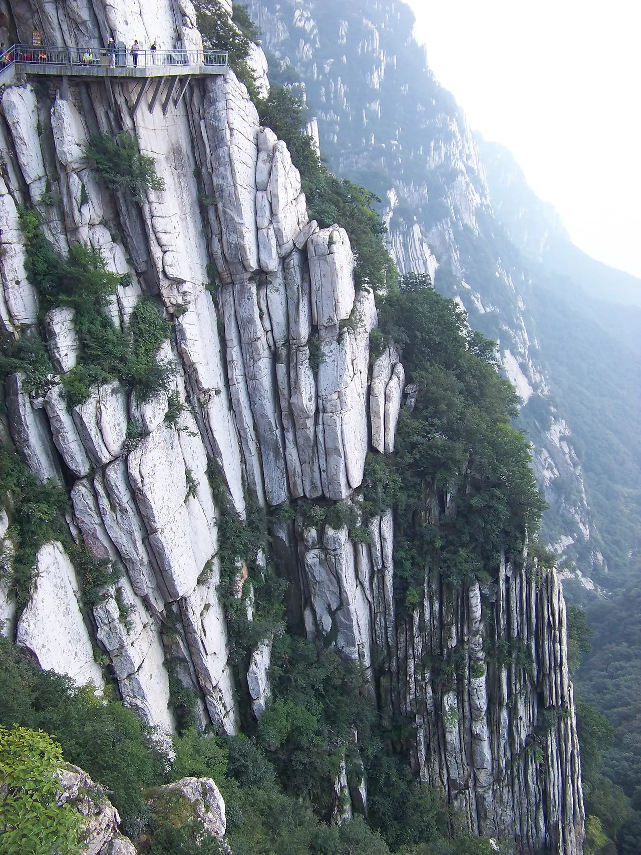 หน้าผาเขาเส้าซื่อ ทางเดินยื่นจากหน้าผาด้านบนซ้ายของภาพ ภาพจาก Wikimedia Commons ผู้ถ่าย Aaron Zhu สัญญา CC BY-SA 3.0 ภาพเก่า ไม่ระบุปี