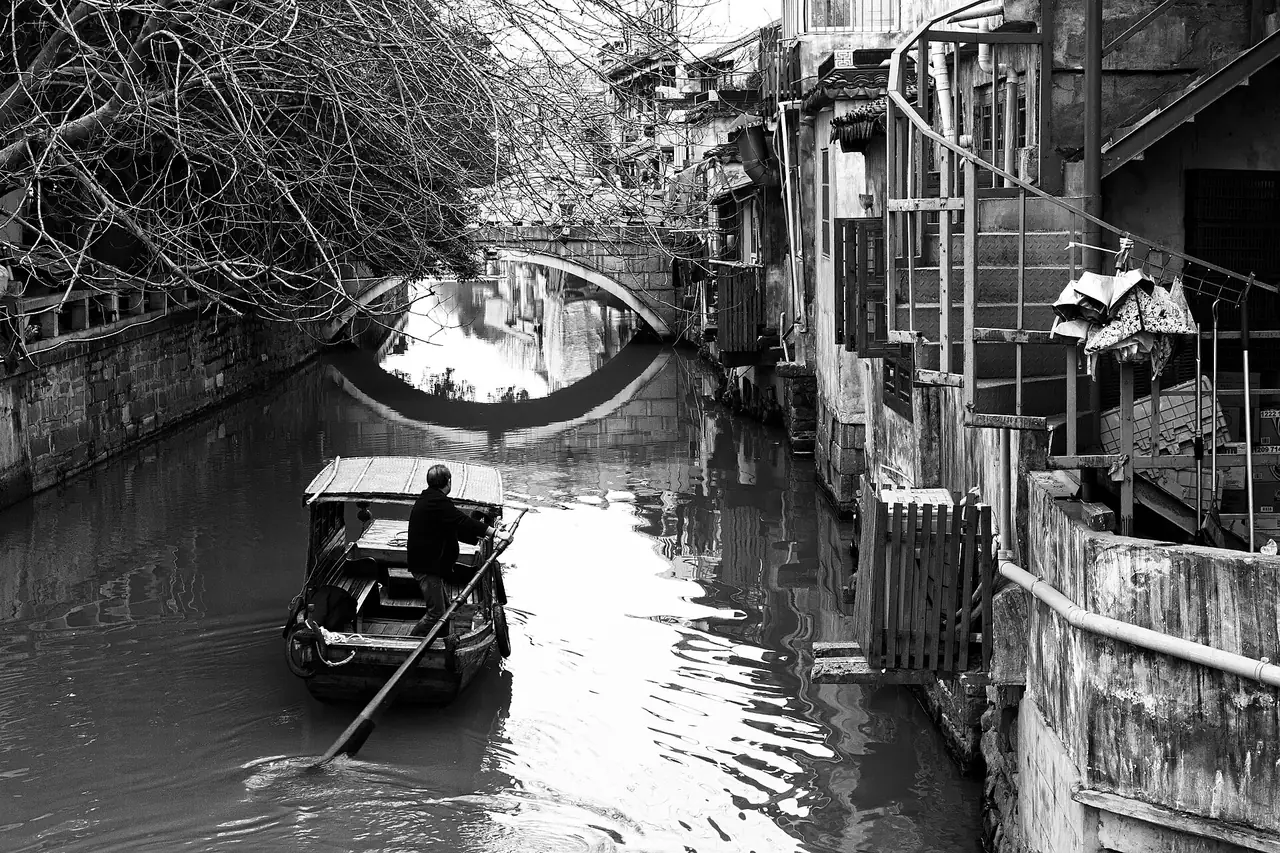 คลองสายเก่าในเมืองซูโจว มีเรือพายผ่านใต้สะพานหิน ภาพขาวดำจาก Wikimedia Commons ผู้ถ่าย Nicolas Vollmer สัญญา CC BY 2.0 ภาพนี้ไม่ได้ระบุว่าเป็นถนนผิงเจียง จึงเป็นภาพประกอบบรรยากาศคลองเมืองเก่า