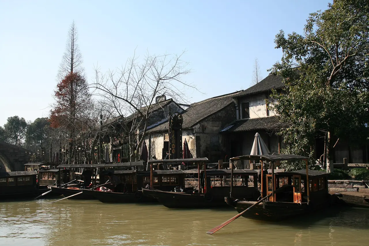 ริมคลองอูเจิ้นมีบ้านไม้ริมน้ำและสะพานไม้ ผู้คนยืนบนสะพาน ภาพจาก Wikimedia Commons ผู้ถ่าย Nablazzz สัญญา CC BY-SA 3.0 ไม่ระบุปีที่ถ่ายในไฟล์ และไม่ระบุว่าเป็นโซนใด