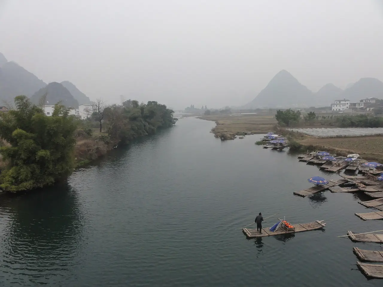 แม่น้ำหยู่หลงกับแพไม้ไผ่จอดริมท่าและเขาหินปูนไกล ๆ ในหมอก ภาพจาก Wikimedia Commons ผู้ถ่าย Annette Teng สัญญา CC BY 3.0 ไม่ระบุปีถ่าย
