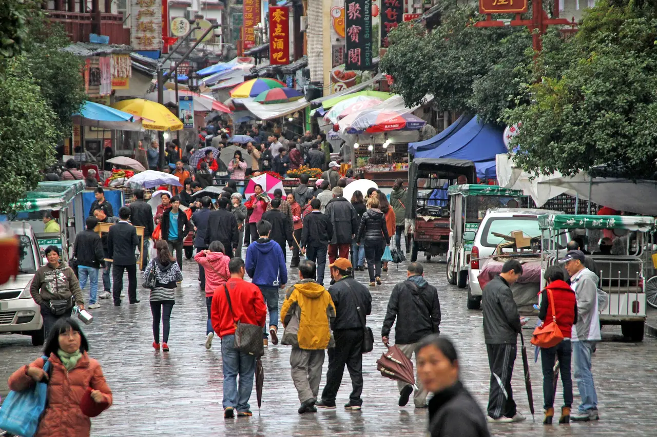ถนนในย่านถนนตะวันตกหยางซั่วหลังฝนตก คนเดินแน่น มีรถสามล้อไฟฟ้าจอดข้างทาง ภาพจาก Wikimedia Commons ผู้ถ่าย Gerd Eichmann สัญญา CC BY-SA 4.0 ถ่ายปี 2555 เป็นภาพเก่า