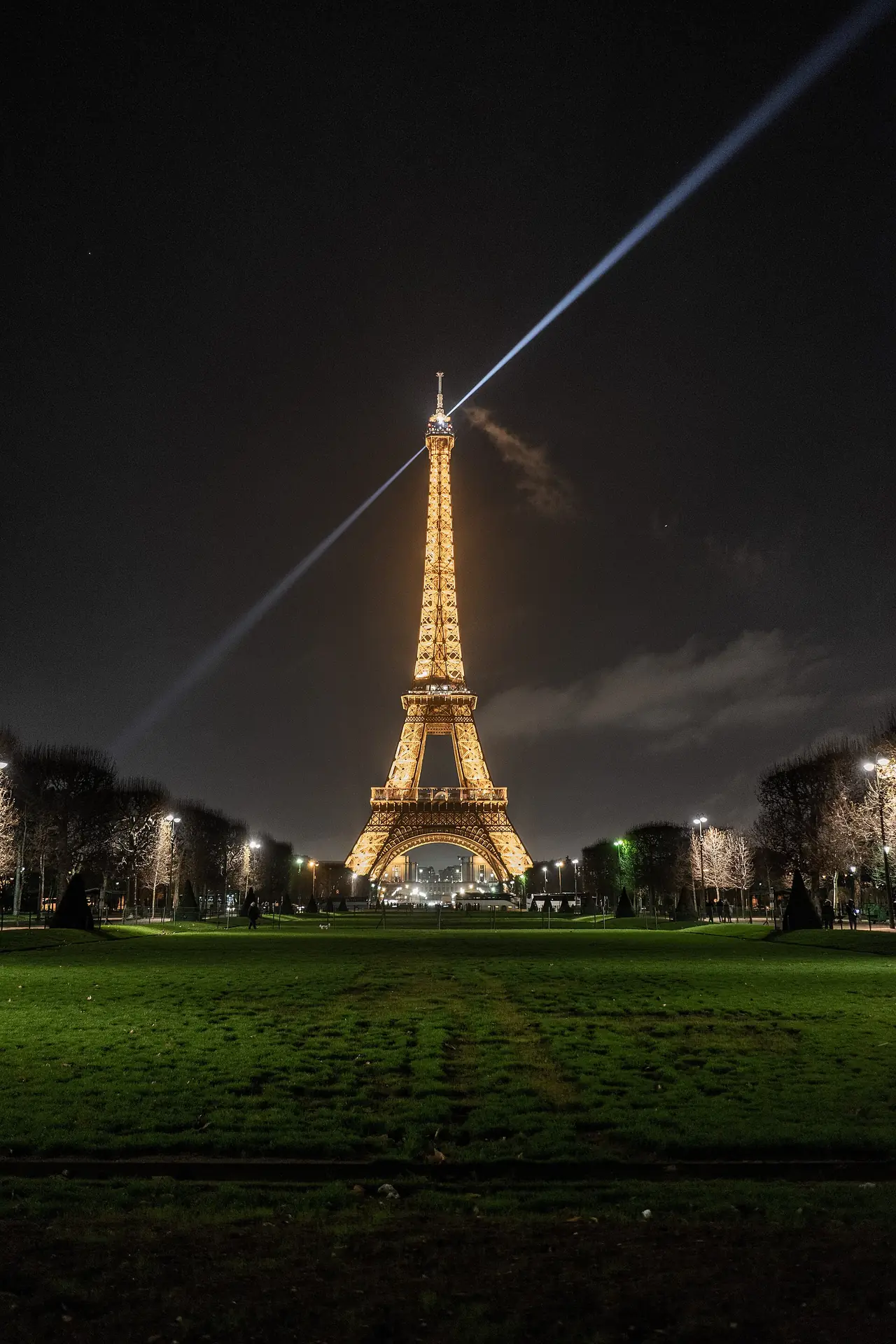 หอไอเฟลยามค่ำพร้อมลำแสงมองจาก Champ-de-Mars ภาพถ่ายจาก Wikimedia Commons