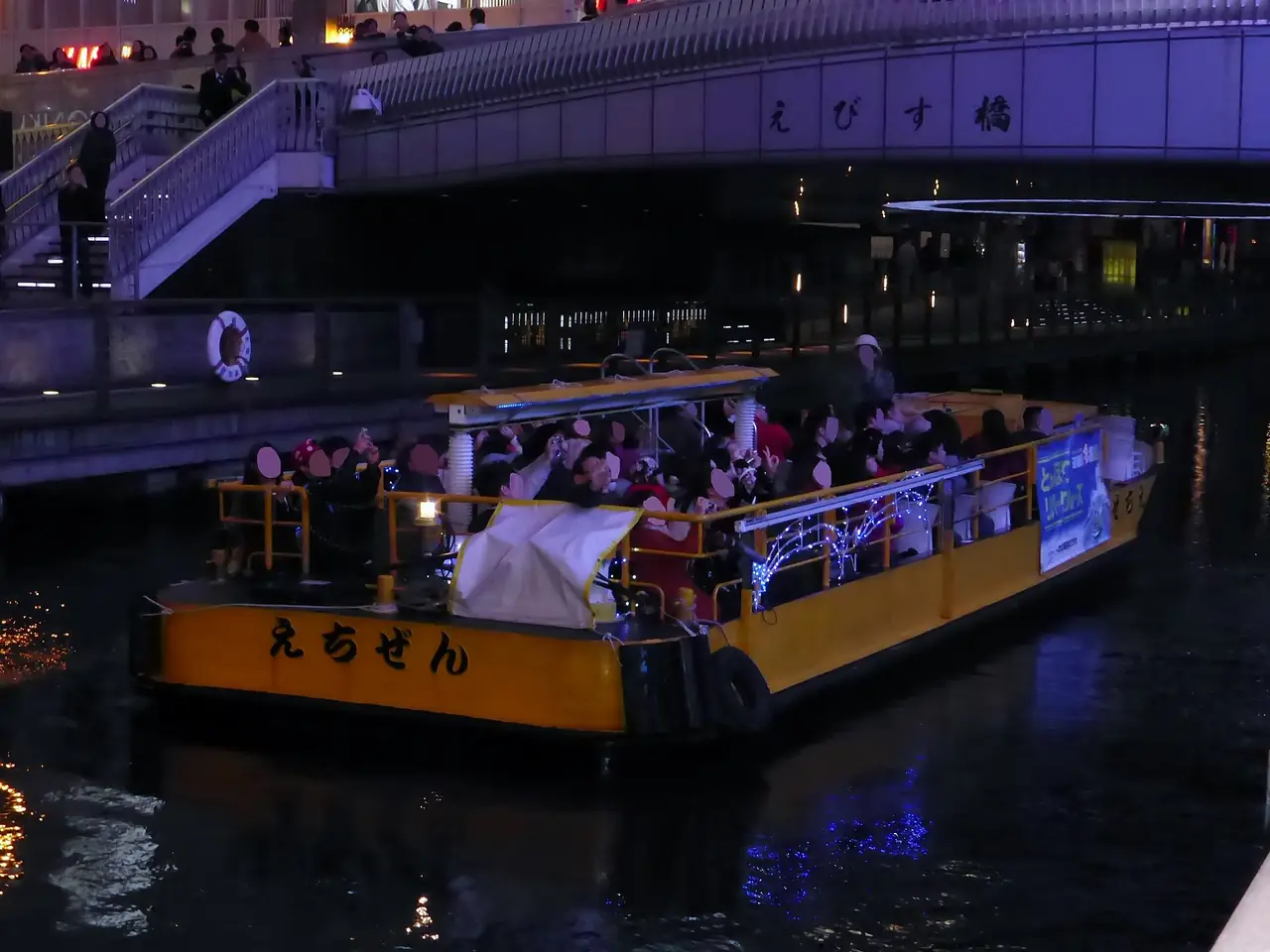 เรือนำเที่ยวในคลองโดทงโบริยามค่ำ ใกล้สะพานเอบิสึ เป็นภาพประกอบ ไม่ยืนยันว่าเป็นเรือของ Tombori River Cruise ภาพจาก Wikimedia Commons ผู้ถ่าย Tokumeigakarinoaoshima สัญญา CC0