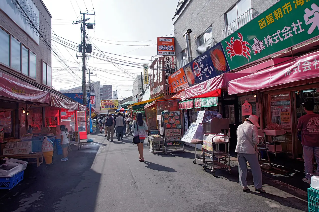 ถนนในตลาดเช้าฮาโกดาเตะ ร้านอาหารทะเลสองข้างทาง ภาพจาก Wikimedia Commons ผู้ถ่าย 663highland สัญญา CC BY 2.5 ภาพเก่า ร้านและป้ายอาจเปลี่ยนแล้ว