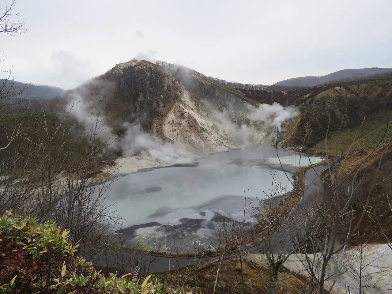 ทะเลสาบโอยุนุมะ มีไอขึ้นจากผิวน้ำ ด้านหลังเป็นภูเขาฮิโยริ ภาพจาก Wikimedia Commons ผู้ถ่าย Calistemon สัญญา CC BY-SA 4.0 ภาพเดือนเมษายน 2566