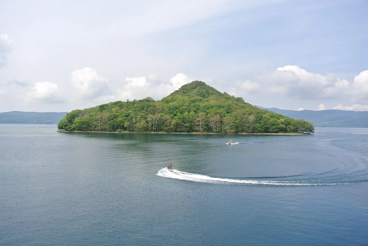 เกาะกลางทะเลสาบโทยะกับเรือเร็ววิ่งบนผิวน้ำ ภาพจาก Wikimedia Commons ผู้ถ่าย Suicasmo สัญญา CC BY-SA 4.0 ภาพวันที่ 8 ส.ค. 2557