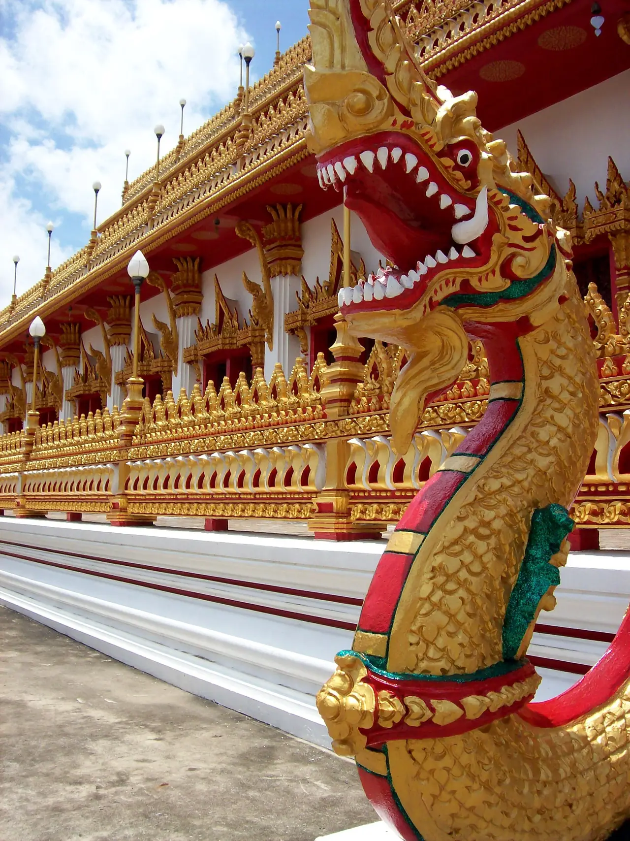 พญานาคสีทองปลายราวบันไดและกำแพงลายทองรอบพระมหาธาตุแก่นนคร ภาพถ่ายจาก Wikimedia Commons