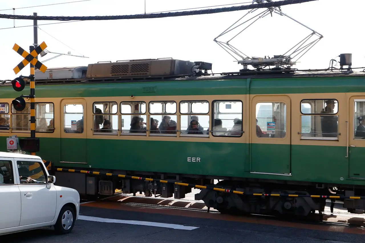 รถ Enoden สีเขียวผ่านทางข้ามใกล้สถานีคามาคุระโคโคมาเอะ (ภาพรถไฟและเครื่องกั้น)