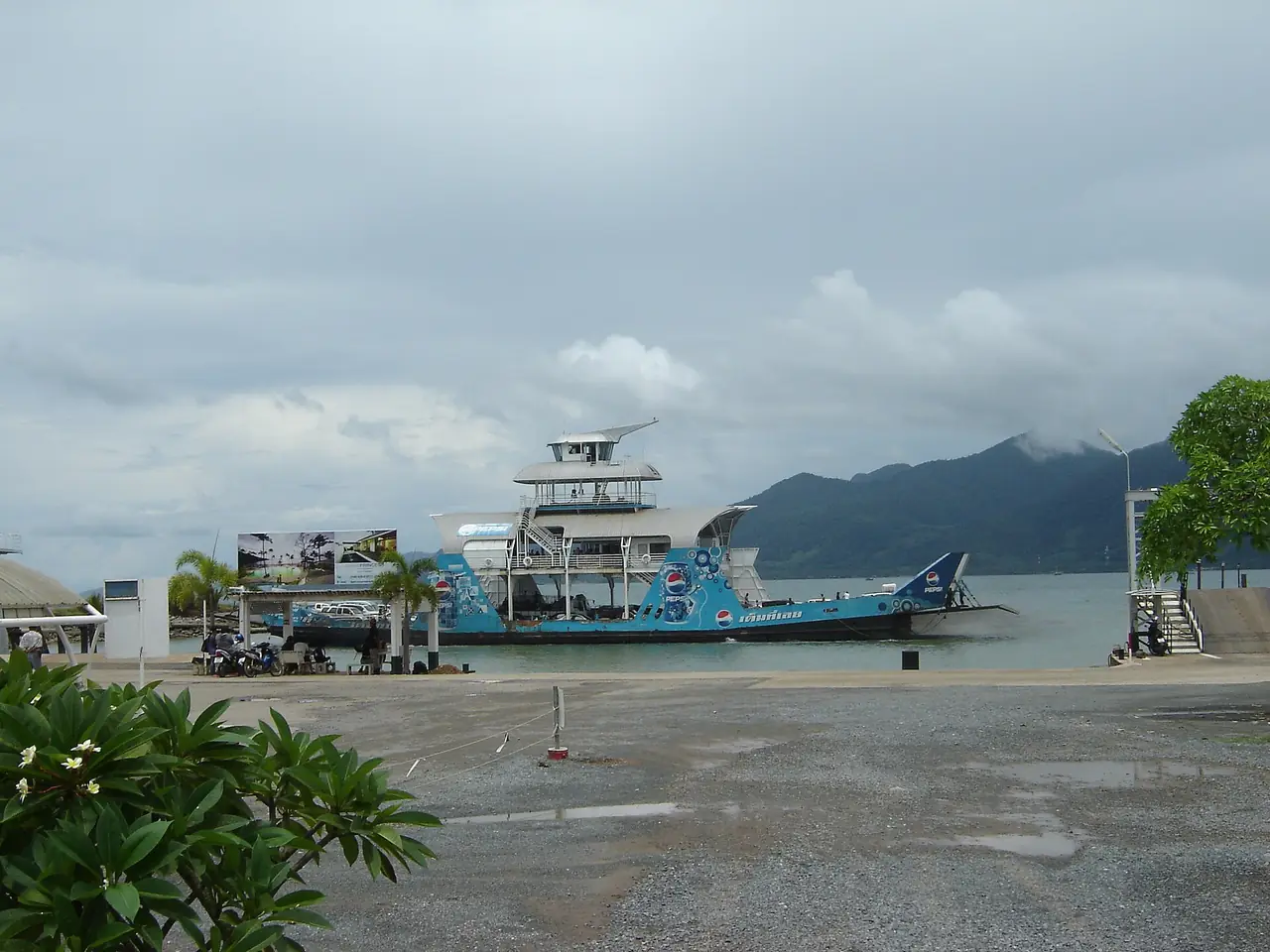 เรือเฟอร์รี่จอดที่ท่าเรือ ท้องฟ้าครึ้มและเทือกเขาอยู่ด้านหลัง ภาพประกอบของ nakhon100 จาก Wikimedia Commons ไม่ได้ระบุท่าเรือที่ถ่าย