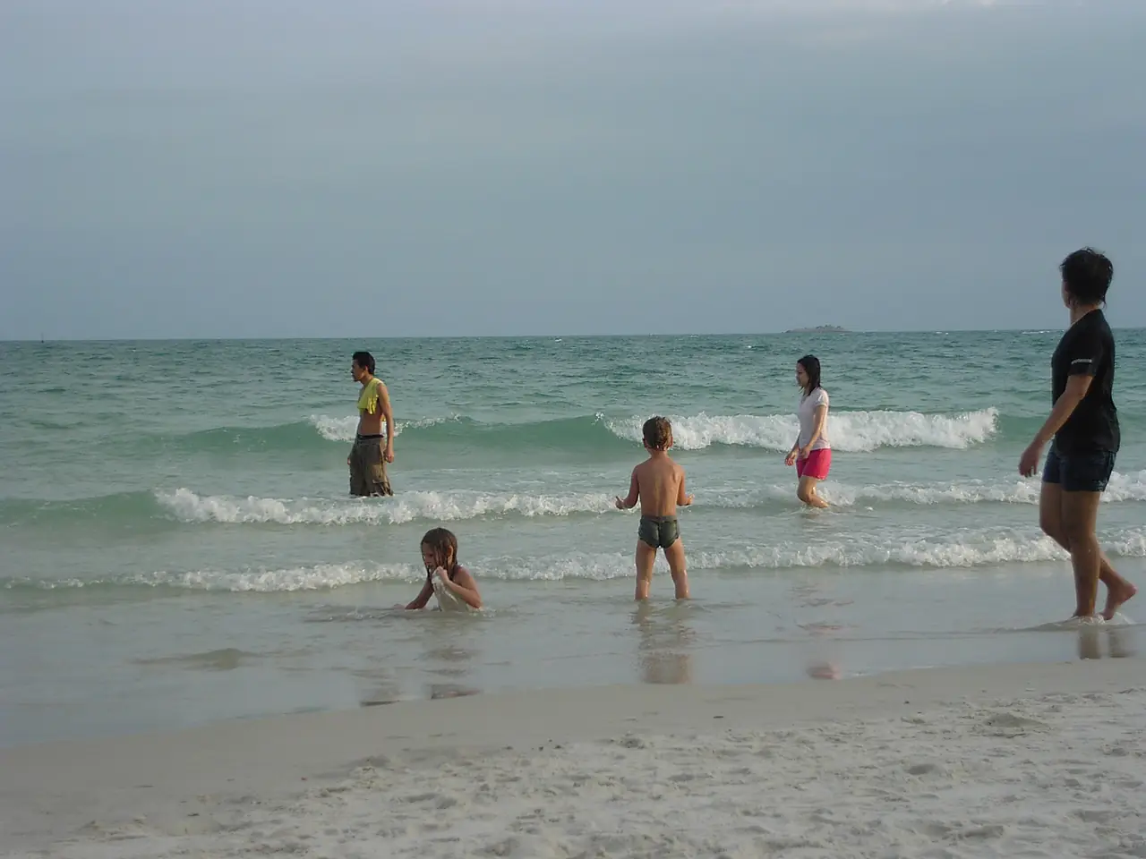 คนเล่นน้ำที่หาดทรายแก้วช่วงแสงเย็น ภาพถ่ายจาก Wikimedia Commons