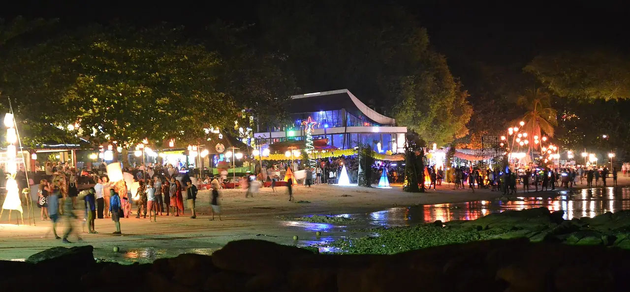 หาดตอนกลางคืนมีร้านที่ประดับไฟและคนเดินเล่น ภาพถ่ายจาก Wikimedia Commons