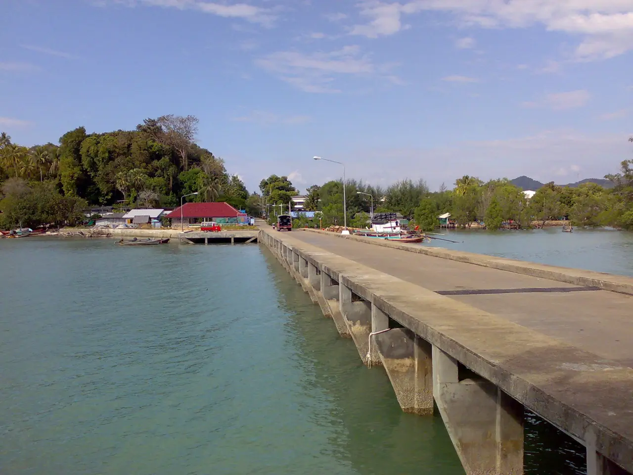 ท่าเรือคอนกรีตยาวยื่นลงน้ำบนเกาะยาวน้อย มีต้นไม้และหลังคาแดงที่ปลายท่า ภาพของ Jaakko H. จาก Wikimedia Commons ตามคำบรรยายภาพบน Commons เป็นท่าเรือที่เกาะยาวน้อย ไม่ได้ระบุท่า