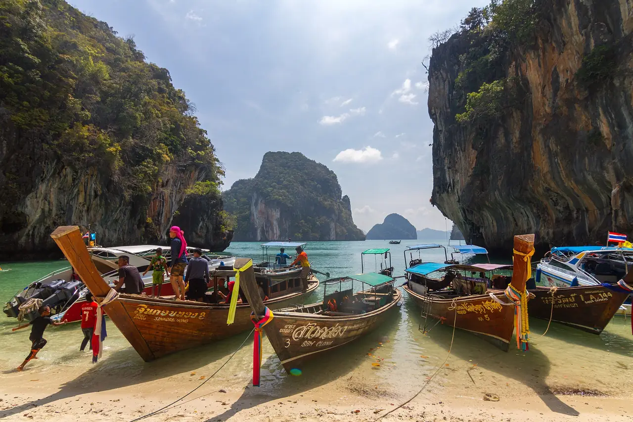 เรือหางยาวไม้หลายลำจอดเทียบหาดทรายที่เกาะละเลาลาดิง มีหน้าผาหินปูนหลังหาด ภาพของ Maksym Kozlenko จาก Wikimedia Commons ถ่ายเมื่อ เม.ย. 2559 ตามคำบรรยายภาพบน Commons