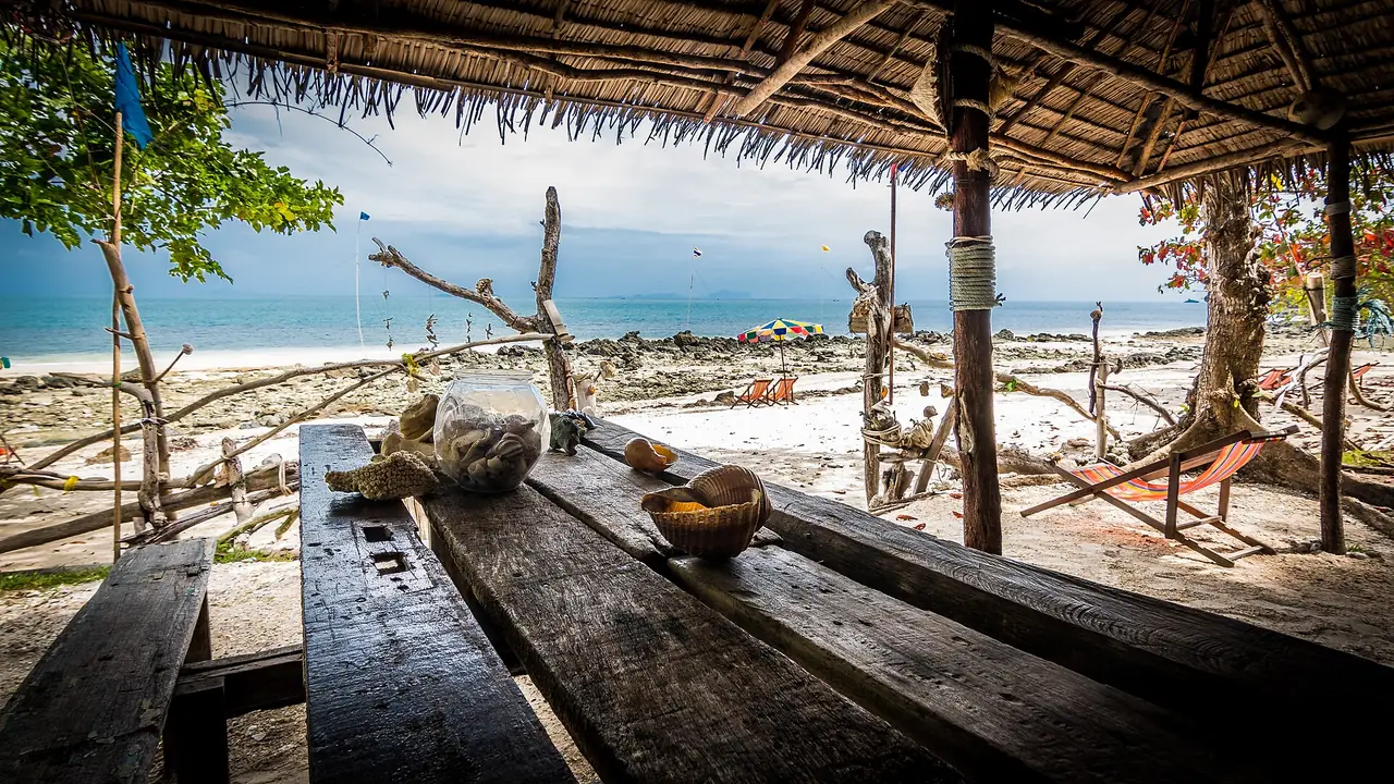 ศาลาริมหาดมุงหญ้า โต๊ะไม้ยาว และหาดทรายขาวหน้าทะเล ภาพของ Tom Ek จาก Wikimedia Commons ตามคำบรรยายภาพบน Commons คือปลายใต้ของเกาะยาวใหญ่ ถ่ายเมื่อ ก.พ. 2560