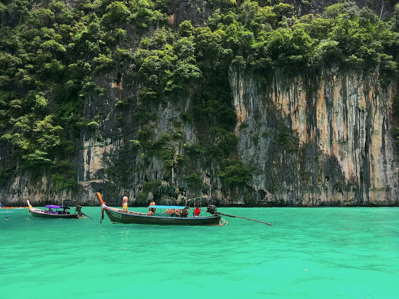 เรือหางยาวในอ่าวปิเละ น้ำสีเขียวมรกตใต้หน้าผาหินปูนบนเกาะพีพีเล