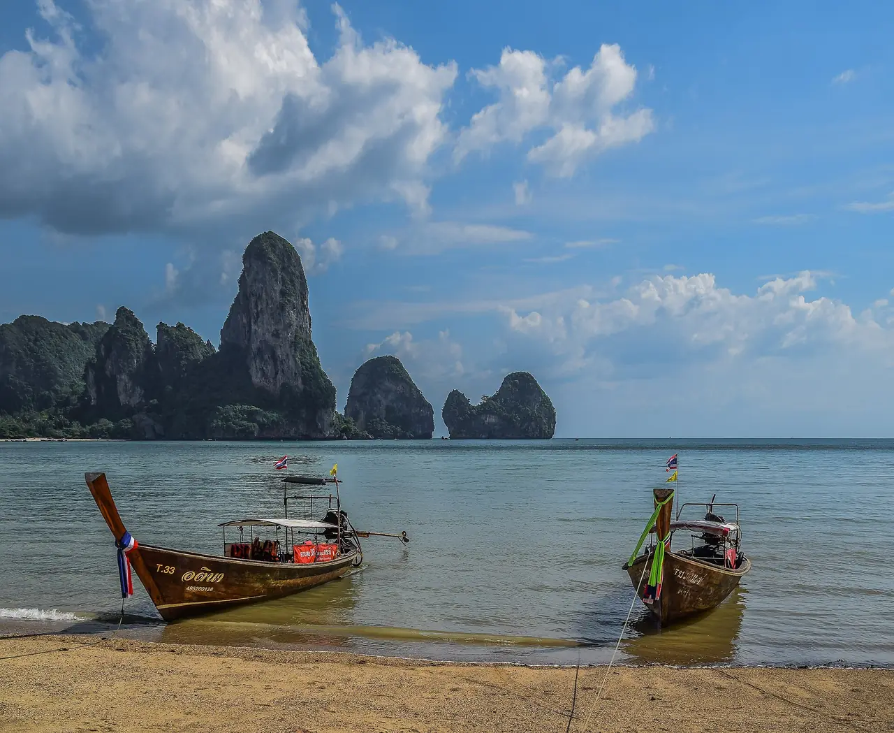 หาดต้นไทร (Ton Sai) บนคาบสมุทรไร่เลย์ มีเรือหางยาวจอดและหน้าผาด้านหลัง ภาพถ่ายจาก Wikimedia Commons