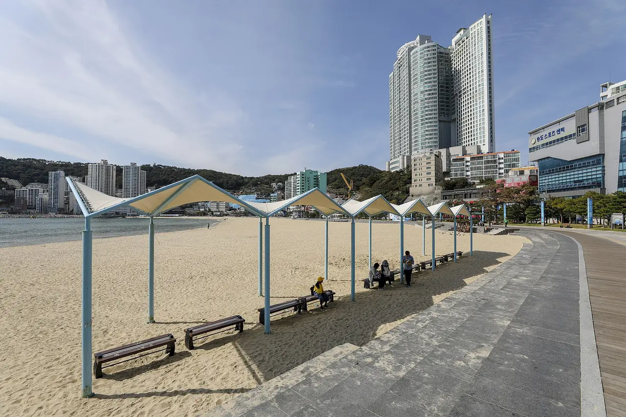 หาดซงโดและทางเดินริมหาด มีศาลาบังแดดแบบผ้าใบและตึกสูงด้านหลัง ภาพจาก Wikimedia Commons ผู้ถ่าย bryan สัญญา CC BY-SA 2.0