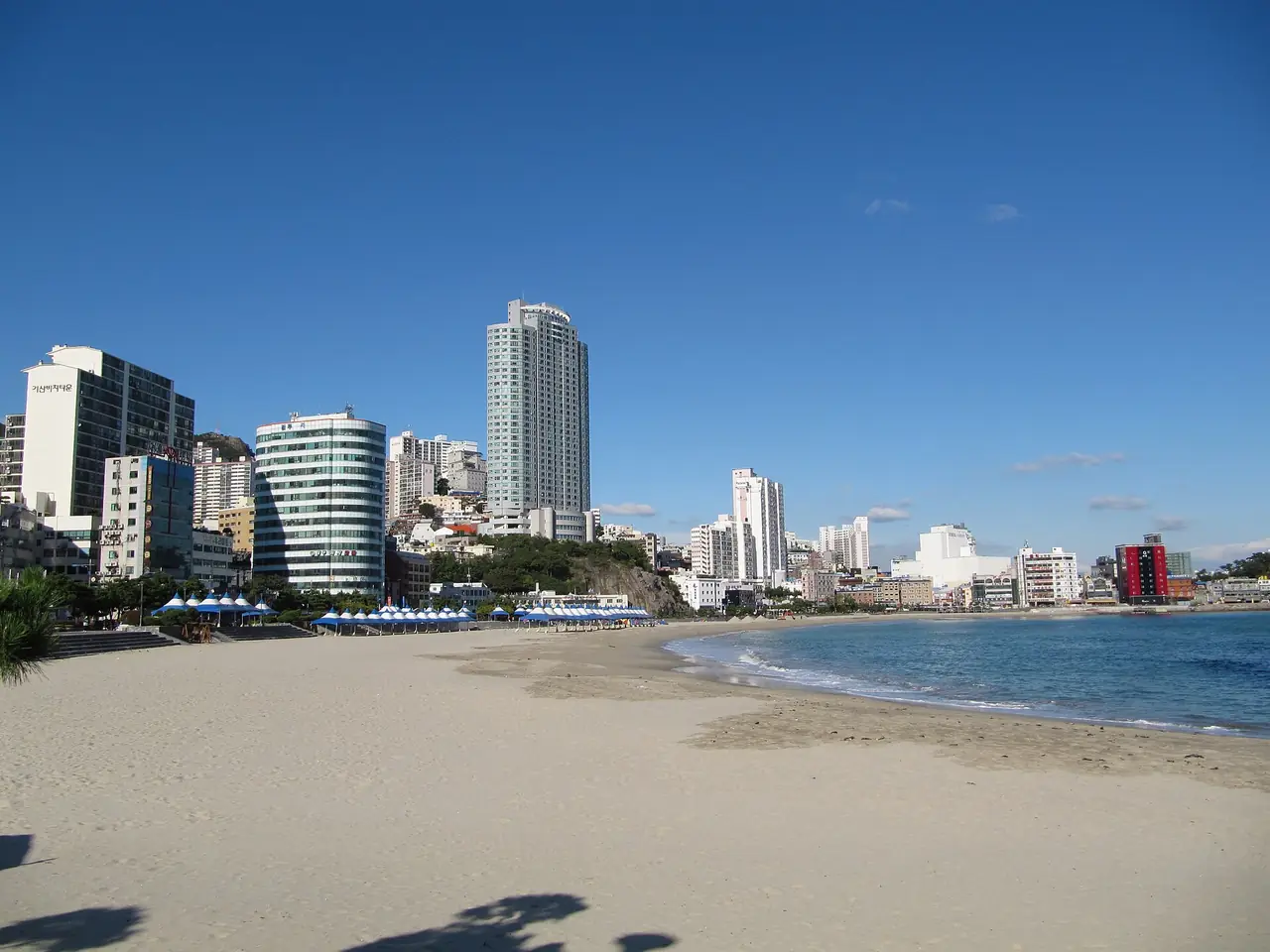 หาดซงโด เขตซอกู ปูซาน ชายหาดโค้งกับอาคารริมหาด ภาพเก่ากว่าการฟื้นหาดบางส่วน ปีที่ถ่ายไม่ระบุ ภาพจาก Wikimedia Commons ผู้ถ่าย Michiel1972 สัญญา CC BY-SA 3.0