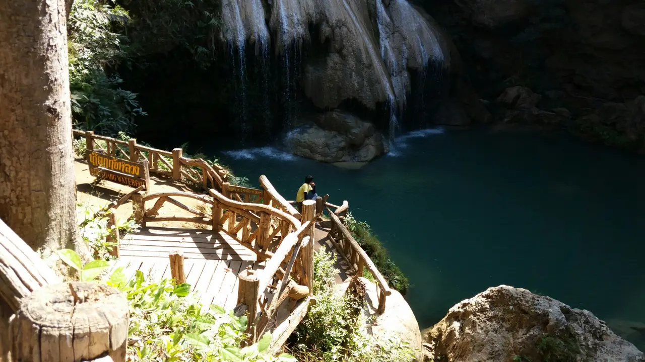 ศาลาไม้และบันไดมองลงแอ่งน้ำสีเขียวเข้มใต้น้ำตกก้อหลวง ภาพของ Piyabongkarn จาก Wikimedia Commons ตามชื่อไฟล์ว่าก้อสวย เขียวมรกต