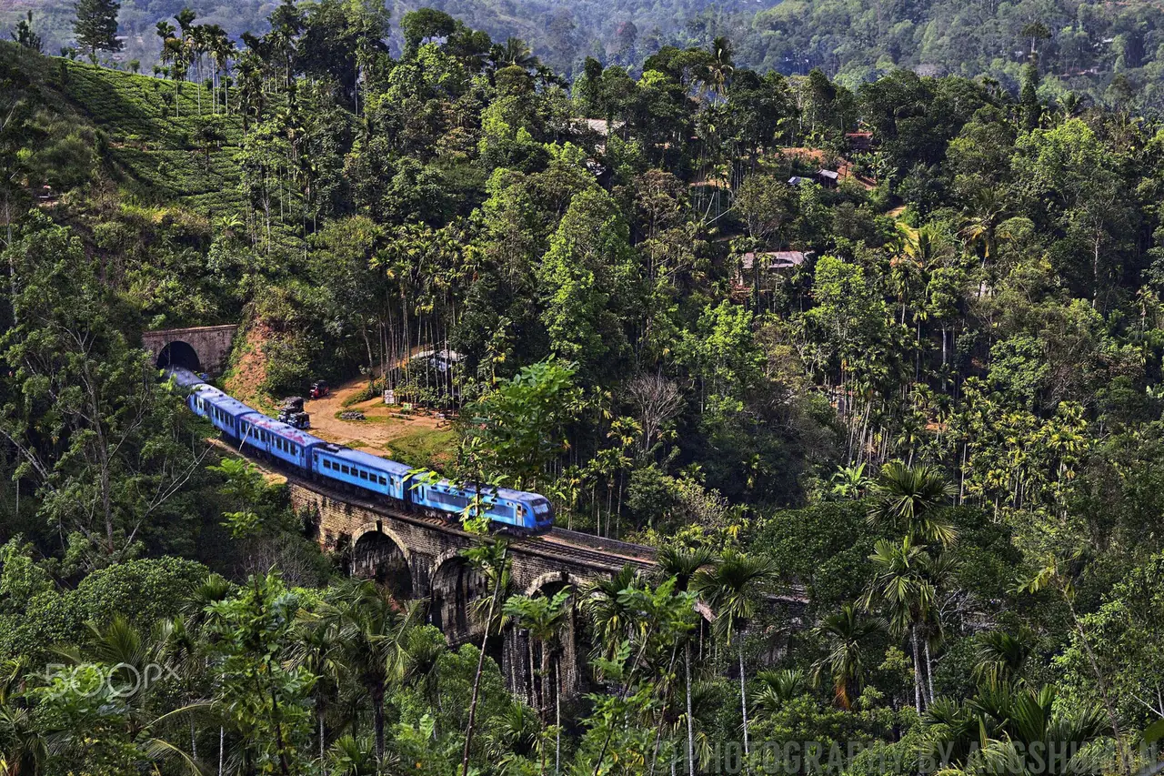 รถไฟสีฟ้าวิ่งบนสะพานเก้าโค้ง มองจากเนินฝั่งตรงข้าม มีลายน้ำของผู้ถ่ายบนภาพ ภาพจาก Wikimedia Commons ผู้ถ่าย Angshuman Chatterjee สัญญา CC BY-SA 3.0 เป็นภาพเก่าก่อนปิดรางจากไซโคลน
