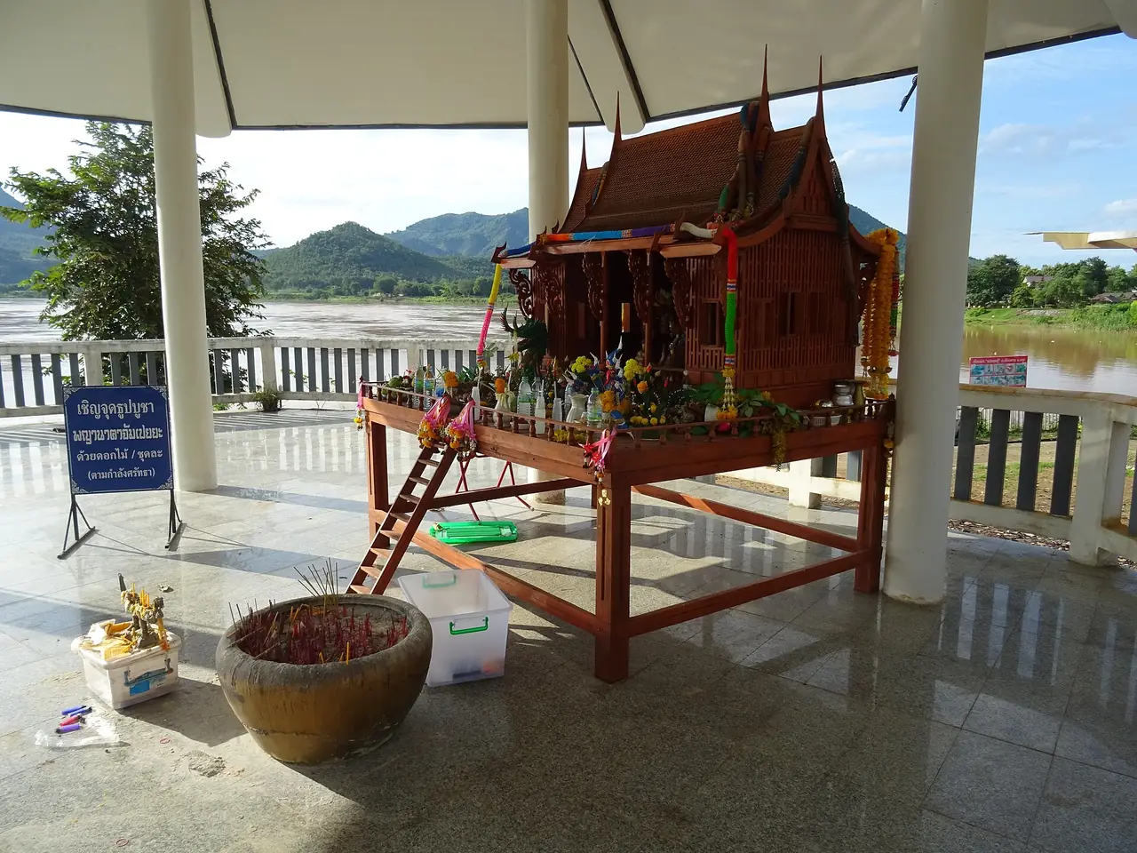 ศาลพระภูมิและโต๊ะบูชาบริเวณแก่งคุดคู้ มองเห็นแม่น้ำโขงเป็นฉากหลัง ภาพถ่ายจาก Wikimedia Commons