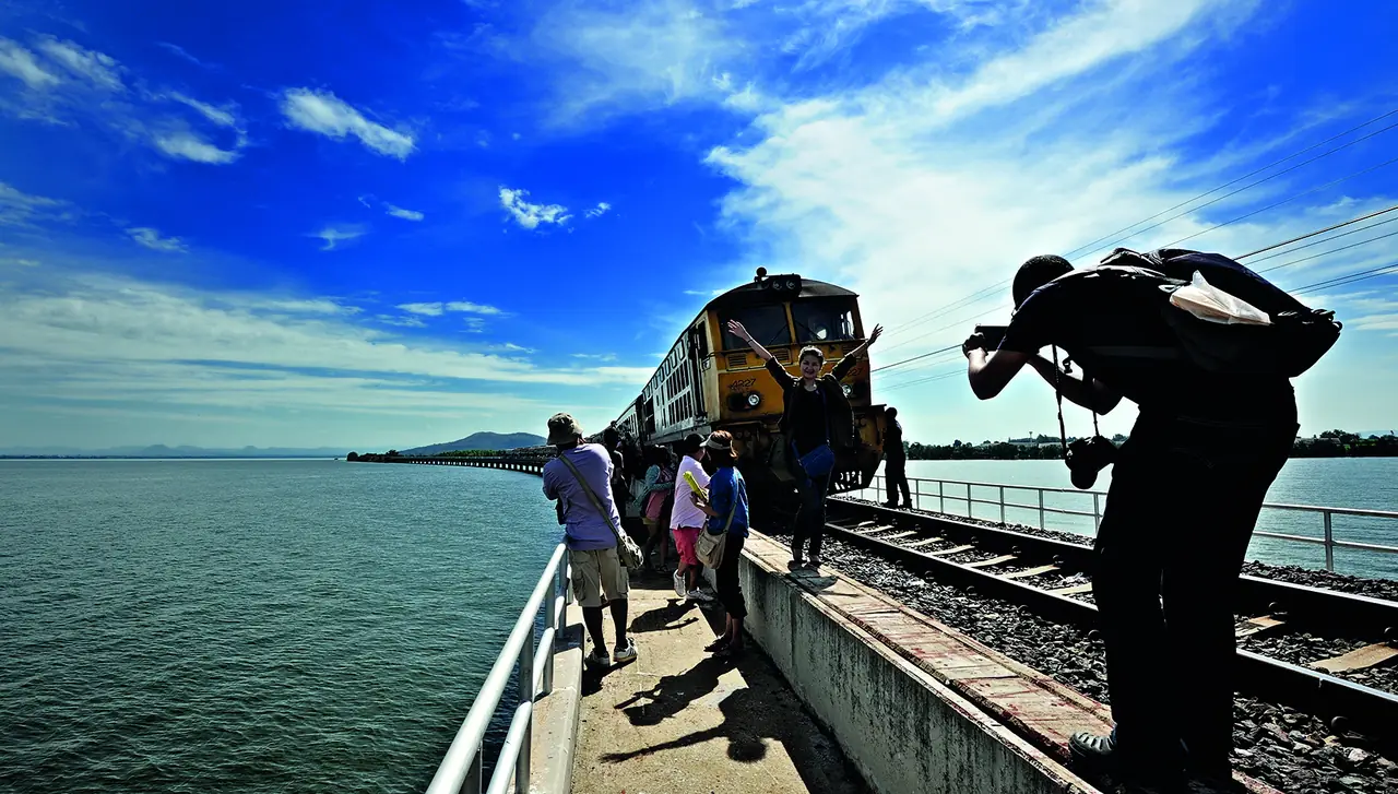 An excursion train stopped on the railway causeway over the Pa Sak Jolasid reservoir with passengers taking photos
