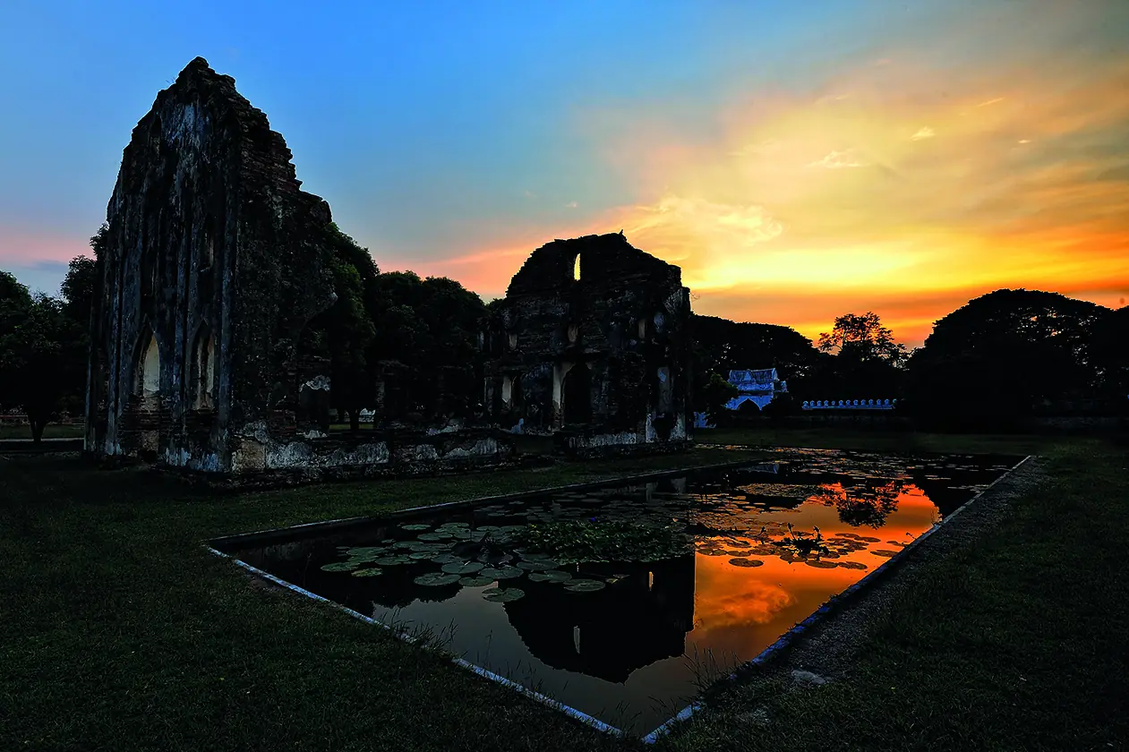 Ruined buildings in Phra Narai Ratchaniwet at sunset with a lily pond in front, Lopburi