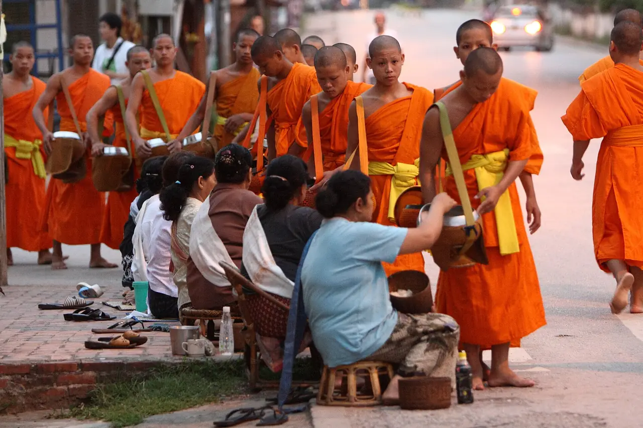 พระภิกษุเดินรับบิณฑบาตและชาวบ้านนั่งใส่บาตรริมถนนตอนเช้า (ภาพบรรยากาศพิธี)
