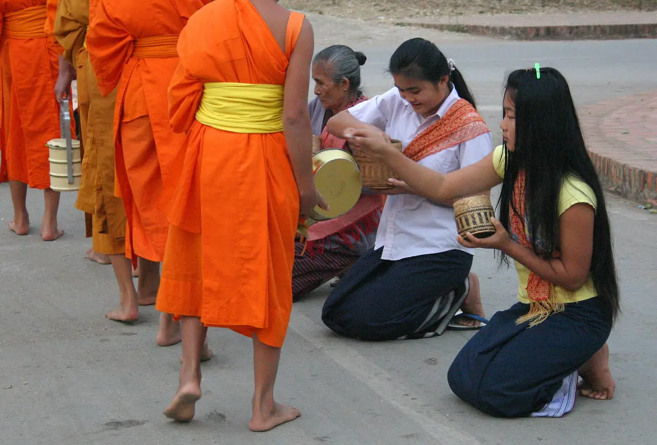 ชาวบ้านคุกเข่าใส่บาตรให้พระภิกษุที่เดินผ่าน (ภาพการใส่บาตร)
