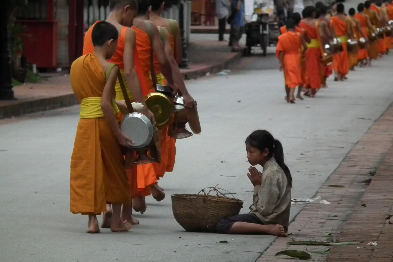 พระภิกษุแถวยาวเดินรับบิณฑบาตริมถนน มีเด็กนั่งรออยู่ข้างทาง (ภาพถนน)