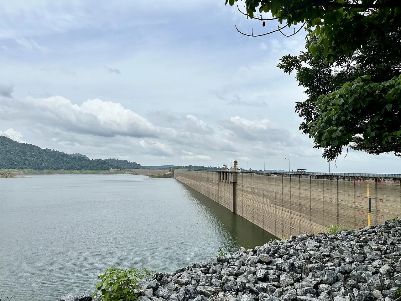 The long concrete face of the Khun Dan Prakarn Chon Dam beside the reservoir, with hills behind