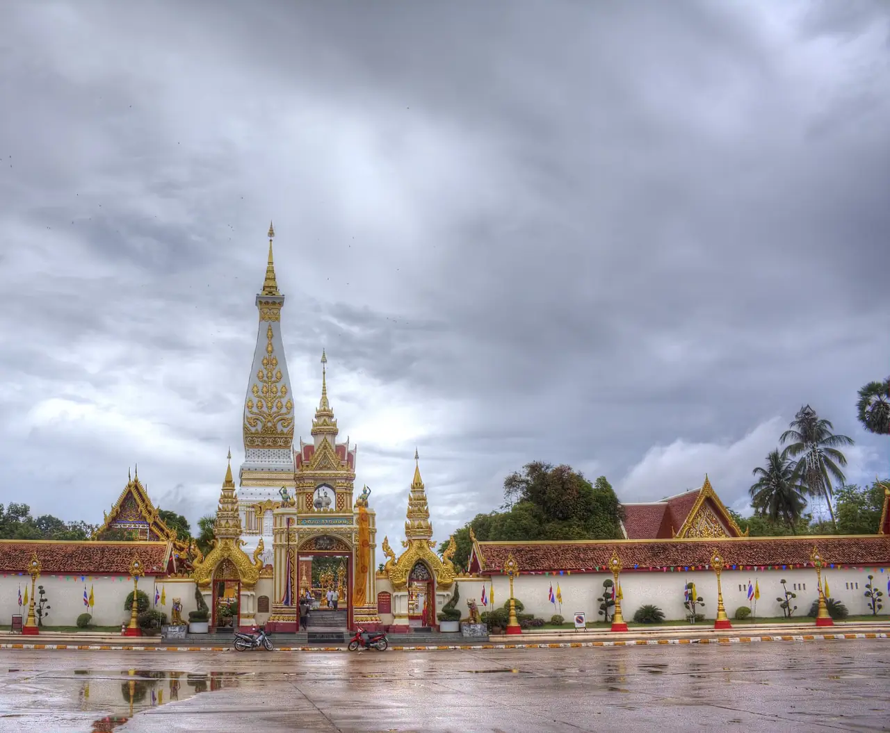 ลานหน้าวัดพระธาตุพนมและซุ้มประตูใต้ท้องฟ้าครึ้ม ภาพของ Hdamm จาก Wikimedia Commons