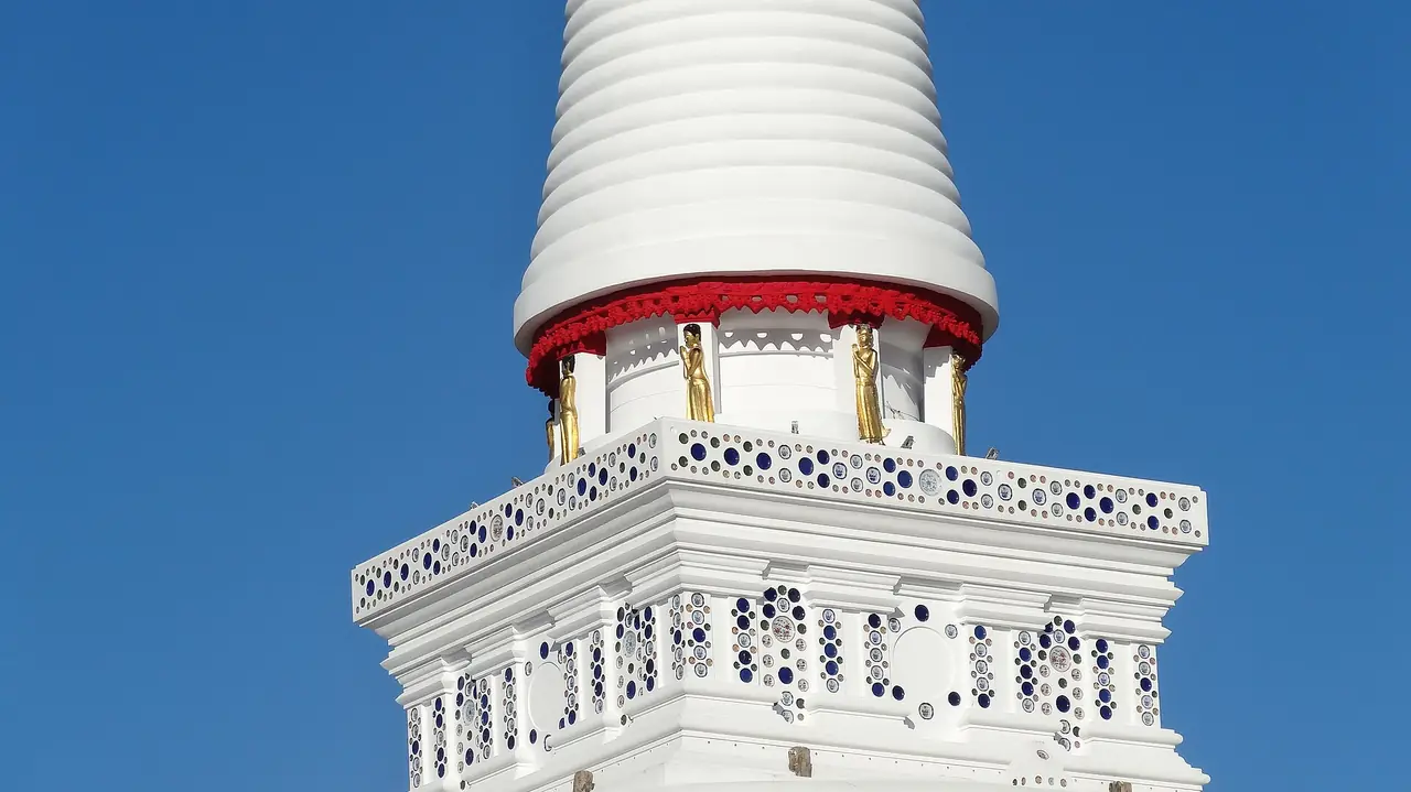 The upper part of a white chedi with a red band and gold figures at Wat Phra Mahathat Woramahawihan