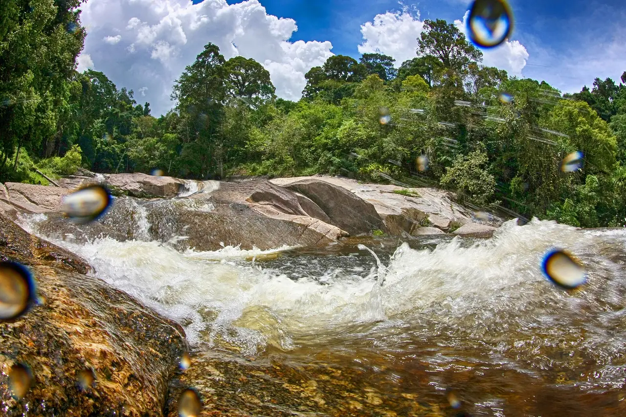 น้ำตกกะโรมไหลผ่านแก่งหินในป่า ภาพของ Chaiyathat จาก Wikimedia Commons ตามคำอธิบายไฟล์เป็นอุทยานแห่งชาติเขาหลวง มีหยดน้ำบนเลนส์ปรากฏในภาพ