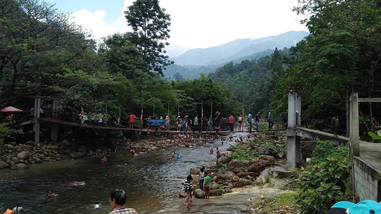 ลำธารตื้นที่มีผู้เล่นน้ำ สะพานข้ามลำธาร และภูเขาด้านหลัง ภาพ CC0 จาก Wikimedia Commons ชื่อไฟล์ระบุหินท่าห้า (Nan Hin Tha Ha) ในอุทยานแห่งชาติเขาหลวง