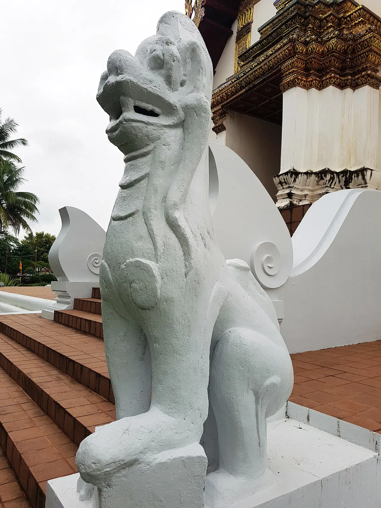 รูปปั้นสัตว์ปูนปั้นสีขาวข้างบันไดอุโบสถ ภาพถ่ายจาก Wikimedia Commons