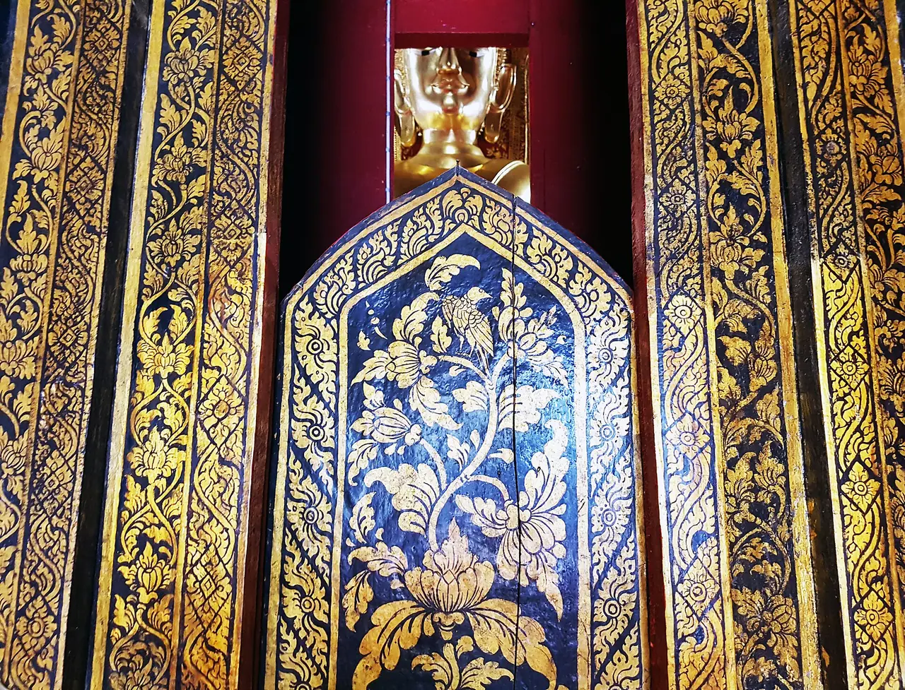 บานประตูลายรดน้ำปิดทองและพระพักตร์สีทองที่มองเห็นอยู่ด้านใน ภาพถ่ายจาก Wikimedia Commons