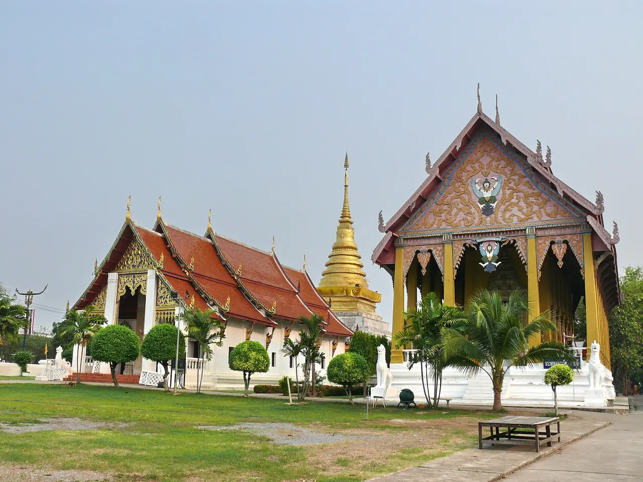 วัดพระธาตุช้างค้ำ มีวิหาร เจดีย์สีทอง และอุโบสถสีเหลืองบนลานหญ้า ภาพถ่ายจาก Wikimedia Commons
